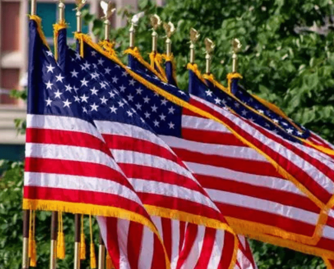 Row of indoor U.S. parade flags with pole hems and gold fringe on gold-tipped poles