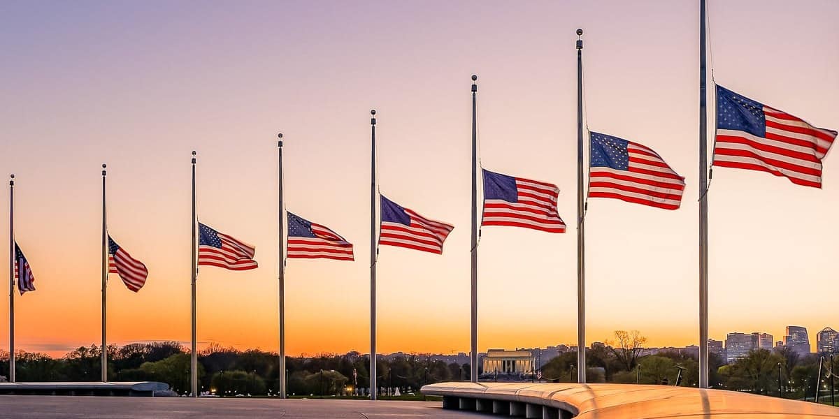 A row of American flags flying at half-staff at sunset