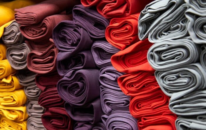 Bolts of folded fabric in yellow, taupe, burgundy, plum, red and grey stacked in rows