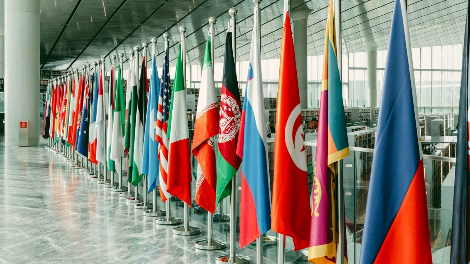 A long row of national flags on indoor poles in a bright modern hall