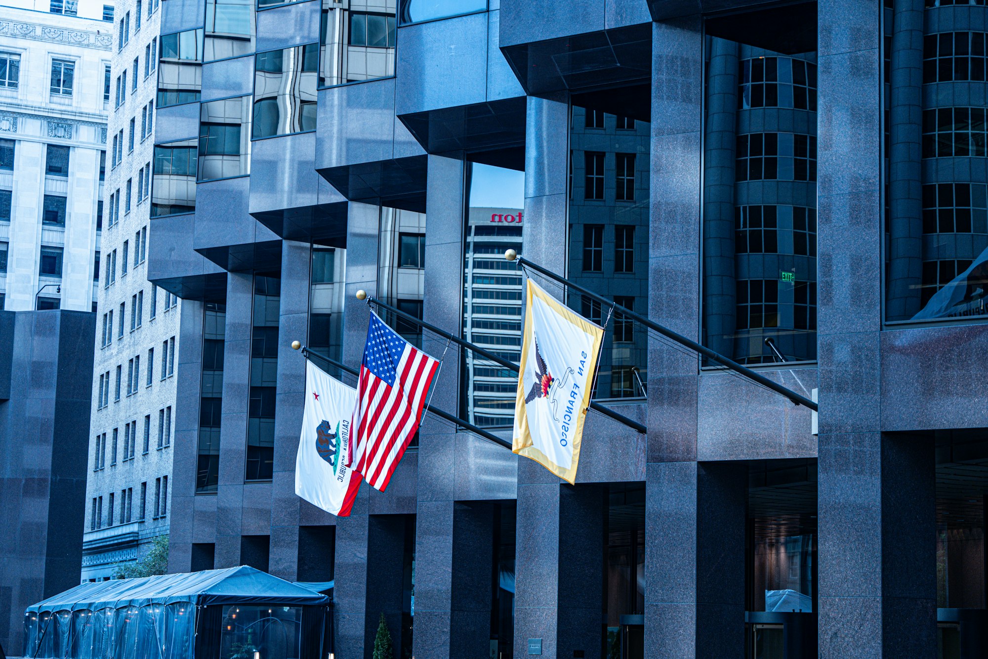 American flag and a city flag on separate poles outside a modern government office building