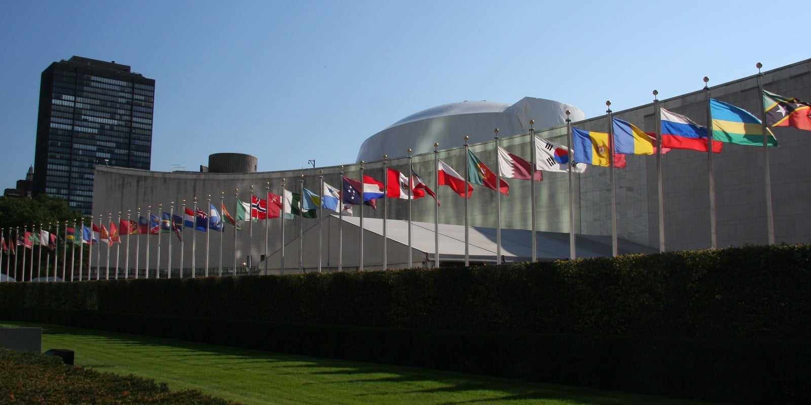 Member state flags on identical poles at identical height along the front of the United Nations General Assembly building on First Avenue in New York