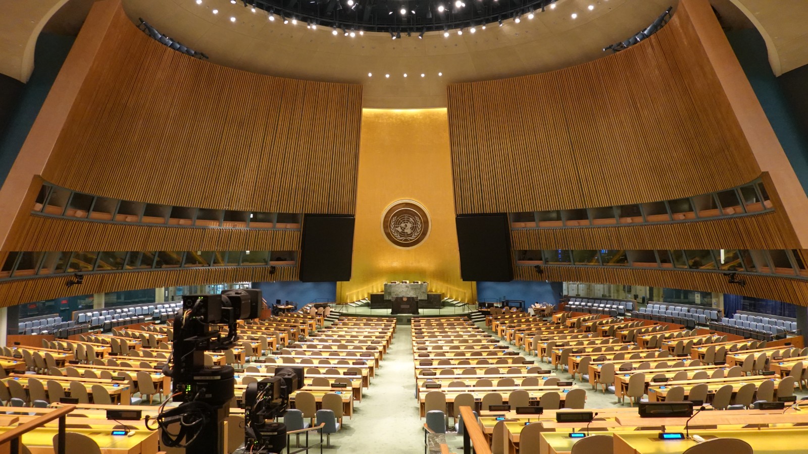 The United Nations General Assembly Hall seen from the rear, empty between sessions, with the gold emblem above the rostrum
