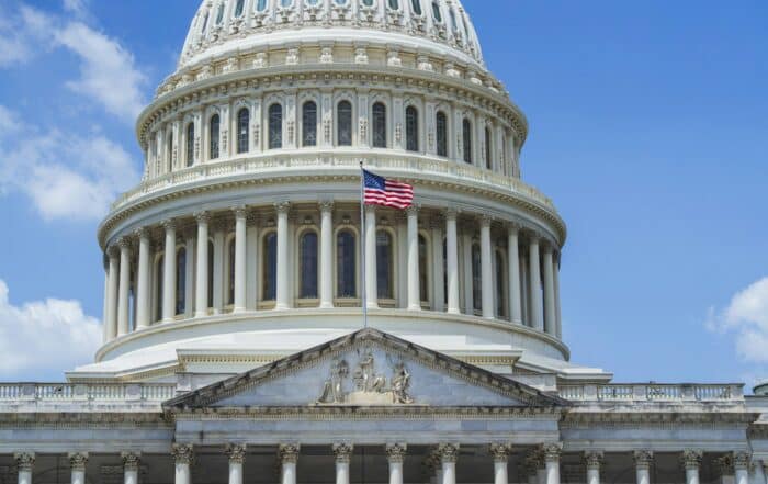 The United States Capitol dome with an American flag flying beside it against a blue sky