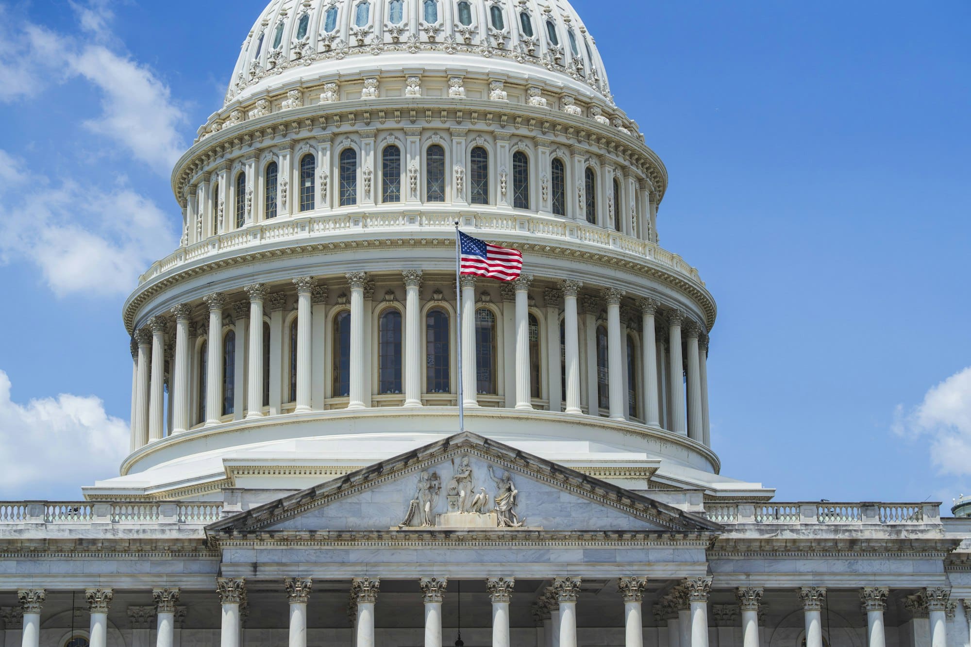 The United States Capitol dome with an American flag flying beside it against a blue sky