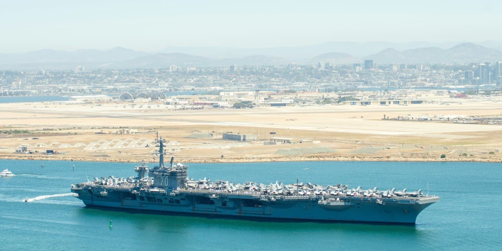 A United States Navy aircraft carrier under way off San Diego with the city skyline behind